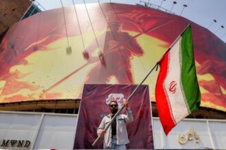 Homem segura uma bandeira do Irã diante de um painel político em Teerã