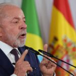 Lula fala diante de microfones com bandeiras do Brasil, Espanha e União Europeia ao fundo
