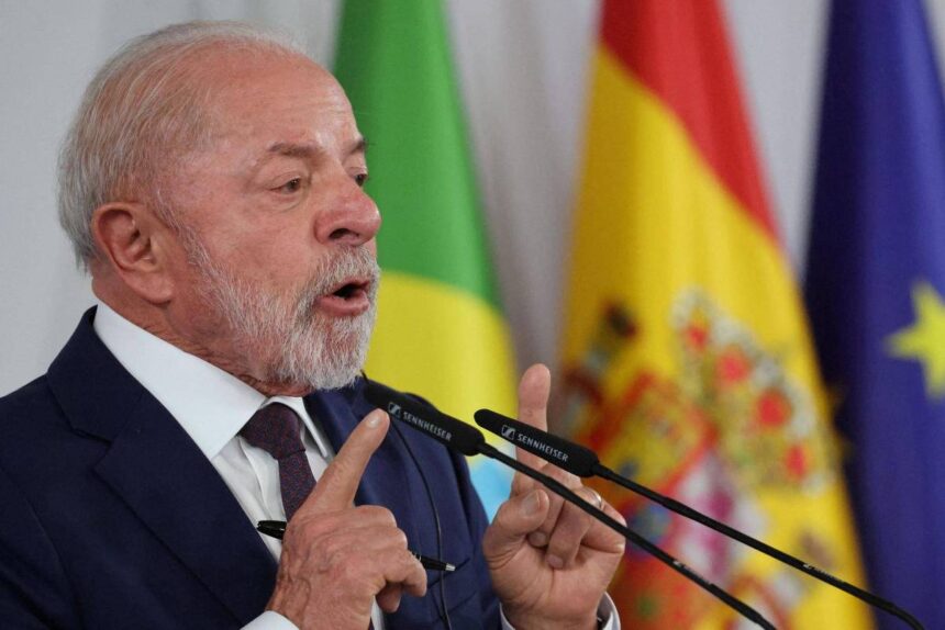 Lula fala diante de microfones com bandeiras do Brasil, Espanha e União Europeia ao fundo